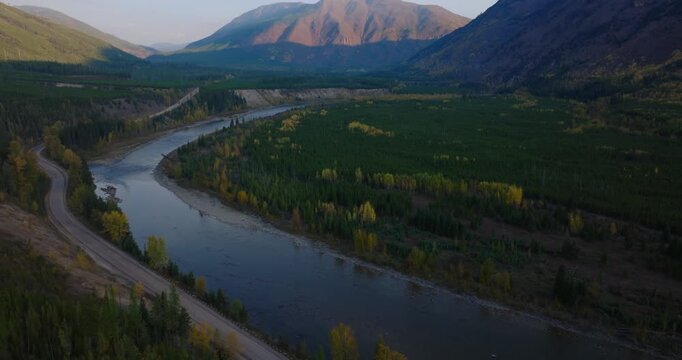 Aerial ascend establishing river flowing below autumn forest in shade of mountain valley