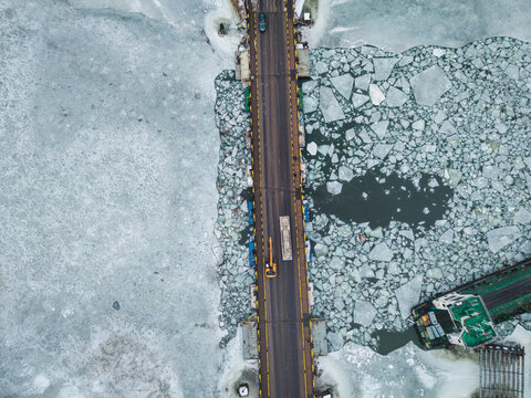 Aerial view of a bridge slicing through a mosaic of icy blues and whites, with a barge navigating the fractured waters of Gdansk, Poland.