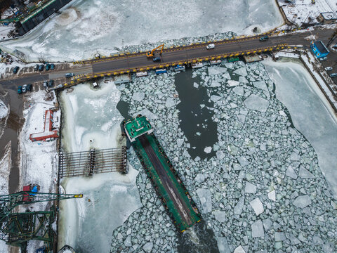 Aerial view of a barge navigating through icy waters near industrial docks, a stark contrast of cold blues and greys under a winter sky, Gdansk, Poland.