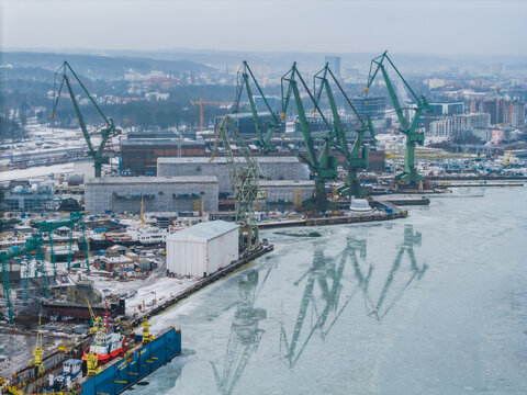 Aerial view of monumental cranes punctuate the skyline over the icy docks and shipyards, a stark industrial tableau against the muted cityscape, Gdansk, Poland.