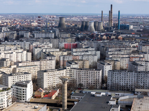Aerial view of a dense cityscape with uniform buildings stretching towards a power plant with towering smokestacks, Bucharest, Bucharest, Romania.