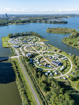 Aerial view of circular campsites nestled amidst serene waters, a vibrant contrast to the distant city skyline, Almere, Flevoland, Netherlands.