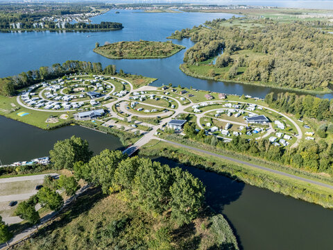 Aerial view of circular camping grounds nestled between waterways and dense foliage, a serene escape in nature's embrace, Almere, Netherlands.