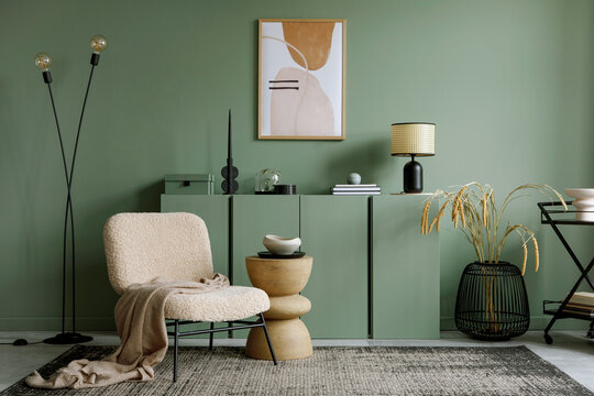 Stylish living room interior design with mock up poster frame, frotte armchair, wooden commode, side table, plants and creative home accessories. Eucalyptus green wall.  Home staging. 