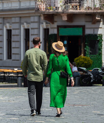 Rear view of fashionable young couple walking holding hands on a sunny day in the old city square. Stylish casual outfits, green dress and straw hat, urban lifestyle, romance, travel and city life in  © Popescu