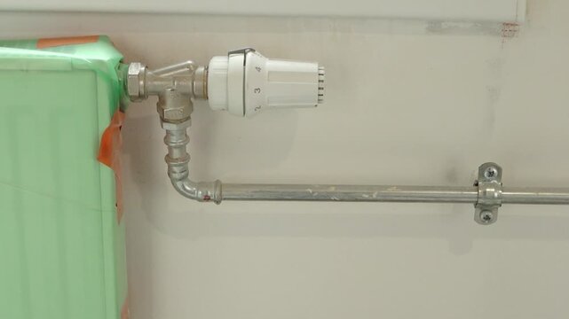Close-Up Of Radiator Valve And Exposed Pipework With Plastic-Covered Radiator During Renovation