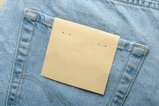 Blank kraft paper label lies on back pocket of light blue jeans and fits fashion branding, clothing tag mockup, and retail use.
