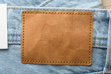 Naklejka na ściany i meble Blank brown leather label on light blue denim jeans with white paper tag, close up mockup for clothing brand identity design