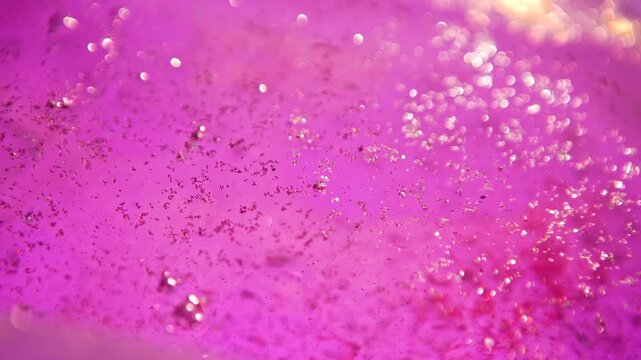 Abstract liquid texture with scattered pink glitter particles and colored glowing highlights. Concepts for beauty and cosmetology, holidays and event, advertising, poster, banner and digital design.