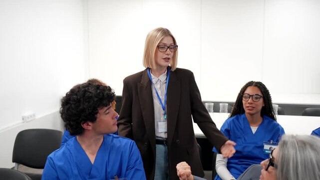 Female lecturer teaching a diverse group of medical students in scrubs during a healthcare training seminar, focusing on professional development and sharing expertise in a modern classroom setting
