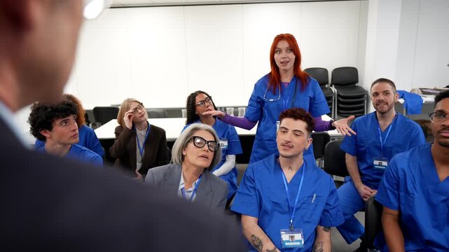 Group of diverse medical students and doctors listening attentively to a female redhead nurse giving a presentation in a hospital conference room during a professional training seminar