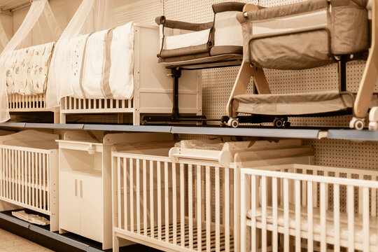 Shelves are filled with various types of baby cribs and bassinets. Parents browse the selection, seeking the right sleeping solutions for their children