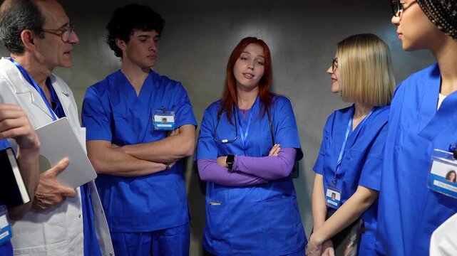 Group of diverse medical professionals, including a senior doctor and young interns, having an important discussion and briefing in a hospital hallway while planning their next steps