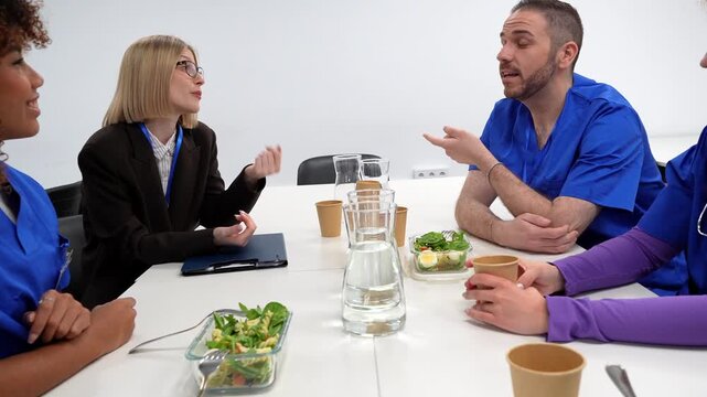 Diverse group of doctors and a hospital administrator discussing work during a healthy lunch break, sharing ideas and smiling in a modern meeting room with a white background