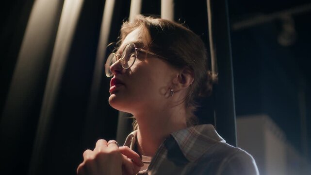 Close up of young adult female comedian with glasses shifting hands restlessly while revising speech standing backstage before live show