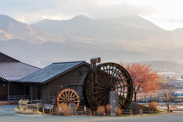 Fototapeta premium Traditional water wheel at Asobo no Sato Kugino Roadside Station with Mount Aso mountains in the background, Kyushu, Japan.