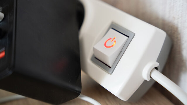 Close up of illuminated power switch with red light on white extension socket indoors