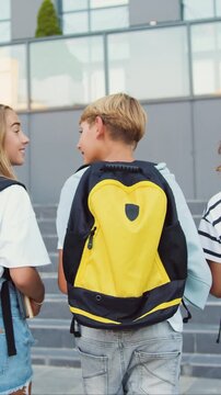 Rear view. Good-looking school child friends climb stairs going to class with backpacks. Boys and girls high school students having fun after school. They are smiling and having fun. Slow motion.