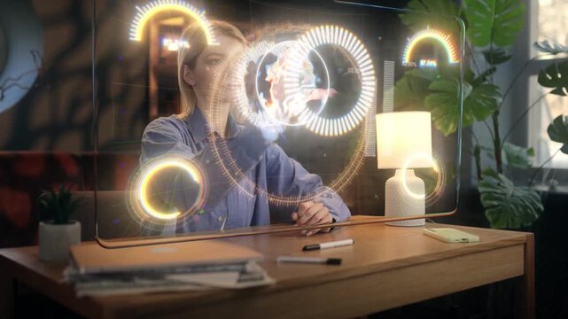 Young woman engineer interacting with futuristic holographic interface at her home office desk