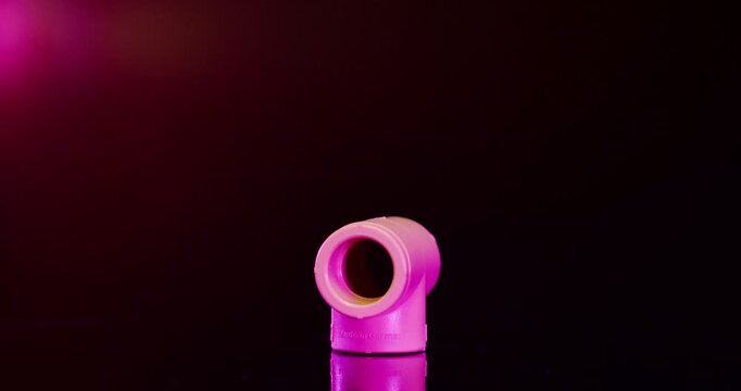 Single pink plastic T-joint pipe fitting and industrial connector against a dark background with red light