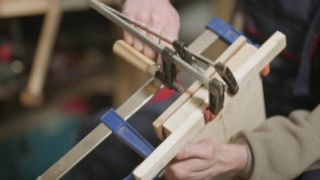 A woodworker carefully uses clamps to secure pieces of wood together. This close-up highlights the meticulous work of wooden craftsmanship.