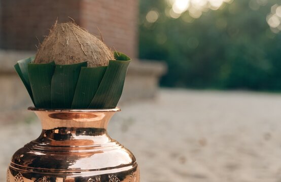 Polished copper water pot with coconut and green leaves. Traditional Indian puja setup background with copy space