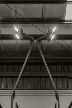 Bright LED floodlights mounted on black metal poles under the ceiling of an indoor padel or tennis sports arena. Industrial lighting.