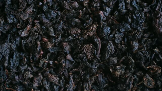 Dark, dry black tea leaves rotating slowly in a macro top view, showing the intricate texture and rich color of the high quality organic beverage ingredient before brewing the hot drink