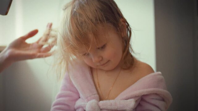 In serene home setting, tender mother gently dries her little one's damp locks with hairdryer, prioritizing child's comfort safety within warmth their family environment, showcasing nurturing moment