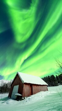 Aurora borealis swirls above a snowy barn near Tromso, Norway, winter night, static tripod timelapse.