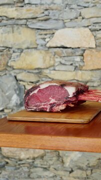 Orbiting shot of raw tomahawk steak on wooden board with stone wall