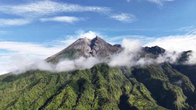 Aerial view footage of Mount Merapi Yogyakarta, beautiful bright blue sky, slightly covered in clouds.