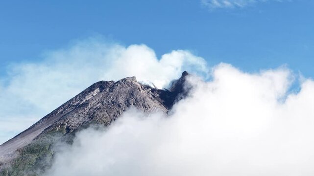 4K aerial footage shows the peak of Mount Merapi in Yogyakarta covered in thick clouds, with clear blue skies.
