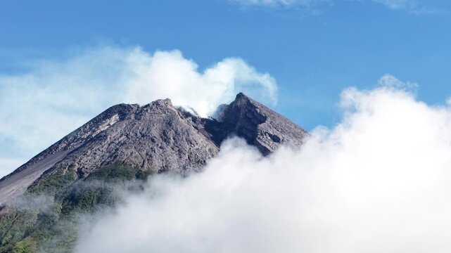 4K aerial footage shows the peak of Mount Merapi in Yogyakarta covered in thick clouds, with clear blue skies.