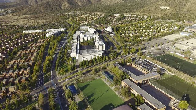 Wide aerial view of the Universidad del Desarrollo campus buildings nestled in a suburban valley near the mountains. Chile, 4K