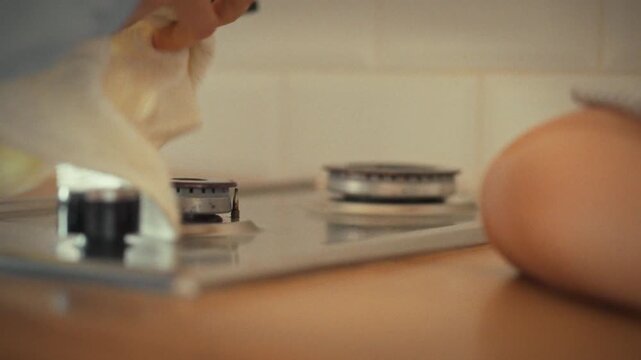 Young housewife scrubs gas stove damp cloth, meticulously removing cooking residue her tidy kitchen. This routine cleaning task exemplifies her dedication to maintaining spotless kitchen environment