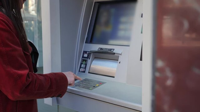 A close-up of a woman using a smartphone with a virtual card at an ATM for contactless cash withdrawal. Mobile payments, NFC technology, and modern banking concepts. High quality 4k footage