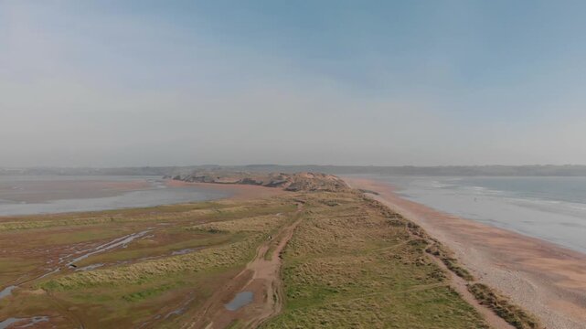 Drone glides over serene coastal landscape, revealing expansive sand dunes and gentle waves, inspiring freedom and natural beauty.