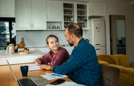 Father helping daughter with homework at kitchen table at home