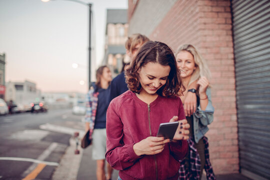 Young woman using smartphone on urban street with friends