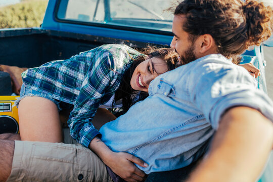 Smiling couple cuddling in pickup truck bed outdoors