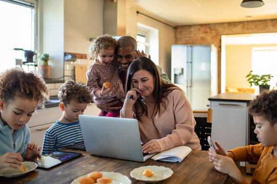 Parents and children using devices at the kitchen table at home