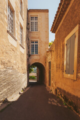 Fototapeta premium A peaceful alleyway welcomes visitors with its warm sunlight reflecting off the aged stone walls. Tall buildings frame both sides, creating a cozy atmosphere of history and serenity