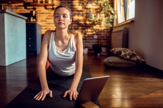 Young woman practicing yoga cobra pose at home with tablet