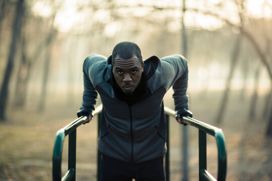 Focused man doing tricep dips on outdoor parallel bars in park