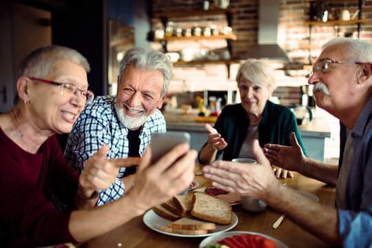 Senior friends using smartphone at home kitchen table