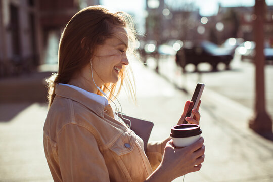 Smiling woman with coffee using smartphone on city street
