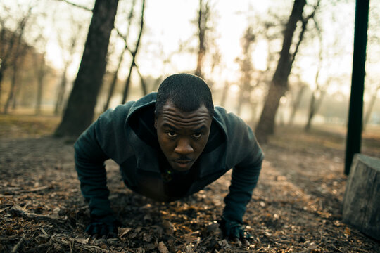 Determined man doing push-ups in forest park at sunrise