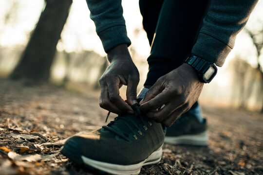 Runner tying running shoe laces on forest trail at sunrise