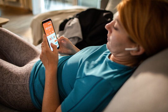 Woman checking fitness app on smartphone at home on sofa